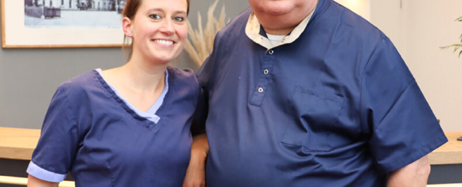 Die Zahnärzte Susanne Rhiem und Dr. Karl-Gottfried Wilhelms stehen gemeinsam an der Praxistheke.