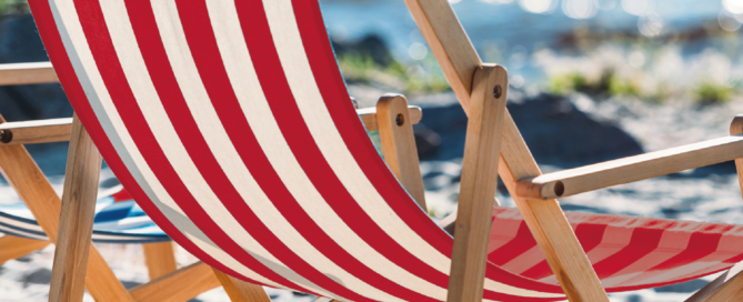 Ein rot-weißer Liegestuhl steht auf dem Sandstrand am Meer.
