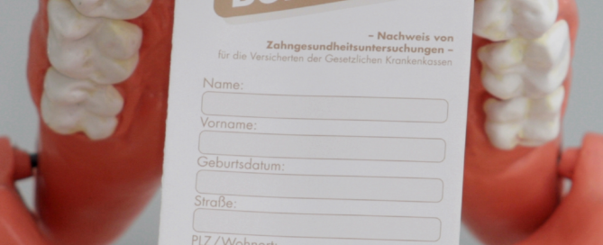 Ein Plastikgebiss hält ein Bonusheft zwischen den Zähnen.
